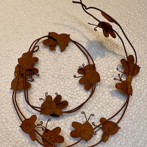 May include: A rusty metal garland with a series of bee-shaped cutouts. The garland is curled into a circle shape.
