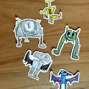 May include: Five die-cut stickers featuring hand-drawn illustrations of whimsical creatures. The designs include a yellow fire-breathing monster, a gray dome-shaped figure, a green two-legged beast, a gray bat-like creature, and a blue winged animal.