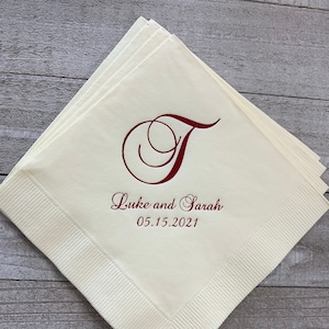 May include: White paper napkins with a red cursive letter T and the text "Luke and Sarah 05.15.2021" printed on them.