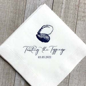 May include: White paper napkin with a blue illustration of an oyster shell and the text "Toasting the Toppings 03.05.2022".