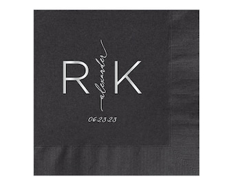 May include: Black paper napkin with silver foil lettering. The letters "R" and "K" are in a large font with the word "alexander" written vertically between the letters. The date "06.23.23" is written below the letters.