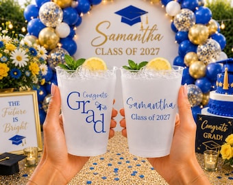 Può includere: Due bicchieri di plastica satinata riempiti con ghiaccio, una fetta di limone e foglie di menta. Un bicchiere presenta la scritta blu Congrats Grad con un'icona di diploma, l'altro mostra Samantha Class of 2027 in caratteri blu.
