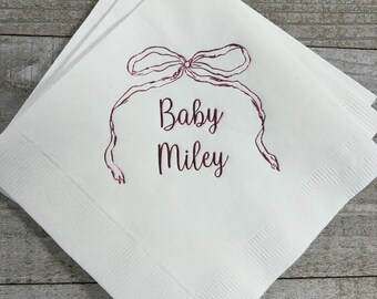 May include: White paper napkins with a pink bow and the text "Baby Miley" printed on them.