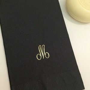 May include: Black cloth napkin with a gold embroidered letter "M" monogram.