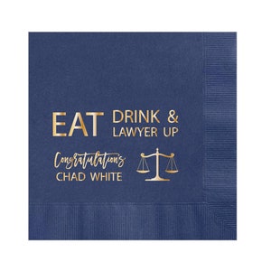 May include: Navy blue paper napkins with gold foil text that reads "Eat Drink & Lawyer Up" and "Congratulations Chad White". A gold scale of justice icon is also included.