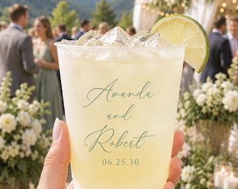 May include: A clear plastic cup filled with a pale yellow beverage, ice cubes, and a lime wedge garnish. The cup features green printed text that reads Amanda and Robert followed by the date 06.25.30 in a simple, elegant font style.