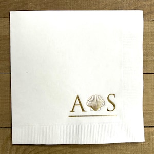 May include: White paper napkin with gold foil lettering "A  S" with a seashell graphic between the letters.
