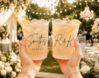 May include: Two clear plastic cups filled with a light-colored iced beverage, ice cubes, a lemon slice, and a sprig of rosemary. One cup features the text The Smiths 03.23.27, and the other cup features the black script lettering R & K.