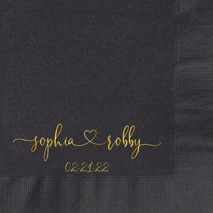 May include: Black paper napkin with gold foil lettering. The text reads "sophia & robby" with a heart symbol between the names and the date "02.21.22" below.