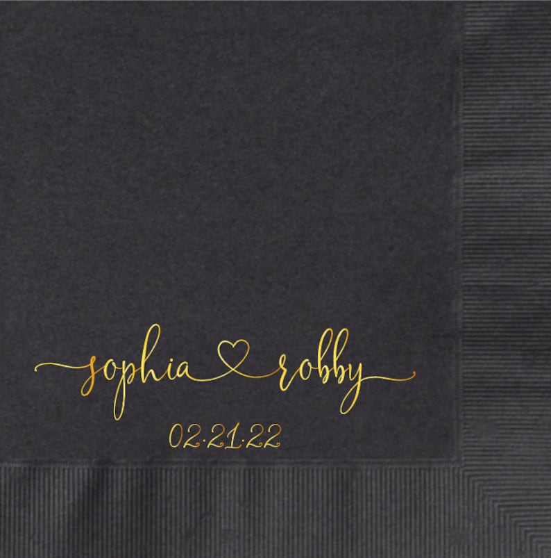 May include: Black paper napkin with gold foil lettering. The text reads "sophia & robby" with a heart symbol between the names and the date "02.21.22" below.