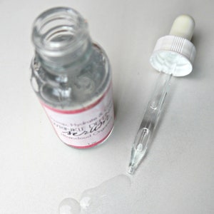 Puede incluir: Una botella de vidrio transparente con un gotero lleno de un l&iacute;quido transparente. La botella tiene una etiqueta rosa y blanca que dice "Hydrate & Glow Wrinkle Defense Serum, Bancloud Organic, 1 oz."