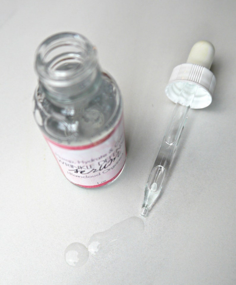 Puede incluir: Una botella de vidrio transparente con un gotero lleno de un l&iacute;quido transparente. La botella tiene una etiqueta rosa y blanca que dice "Hydrate & Glow Wrinkle Defense Serum, Bancloud Organic, 1 oz."