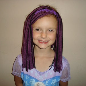 May include: A young girl with long, purple and black yarn braids. She is wearing a light purple and blue dress with a snowflake pattern.