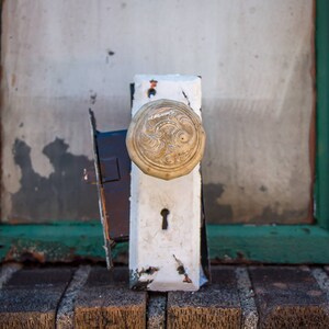 May include: A white door knob with a decorative brass plate and a keyhole. The knob has a floral design and is mounted on a wooden door.