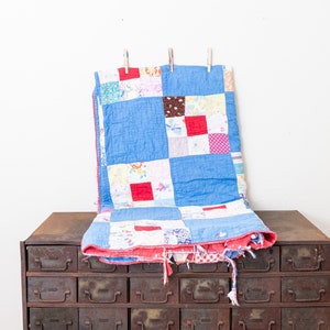 May include: A blue and red patchwork quilt with a frayed edge is draped over a vintage metal cabinet with multiple drawers.