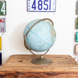 May include: A blue globe with a metal stand sits on a wooden table. The globe is surrounded by vintage license plates with numbers and state names.