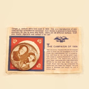 May include: A vintage campaign button featuring a black and white photo of William Howard Taft and Theodore Roosevelt. The button is red, white, and blue with a heart design. The text "The Campaign of 1908" is printed on the card.