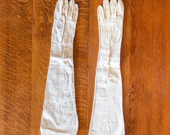 May include: A pair of long white gloves with button detailing. The gloves are made of a smooth, soft material.