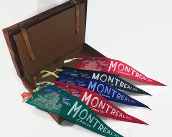 Könnte beinhalten: Eine Sammlung von Montreal-Wimpelfahnen in Rot, Blau und Grün, mit weißem Text und Gebäudeillustrationen. Die Fahnen werden in einem offenen braunen Lederetui mit Griff und Verschlüssen präsentiert.