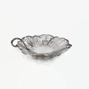 May include: A silver decorative serving dish with a delicate, openwork design and a single handle. The dish is made of metal and has a scalloped edge.