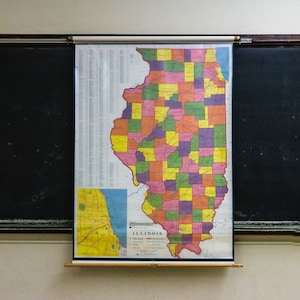 May include: A vintage map of Illinois, divided into counties, with each county colored in a different shade of yellow, orange, red, pink, purple, green, or blue. The map is mounted on a roller and is hanging on a wall.