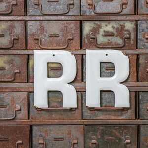 May include: Two white metal letters, "R" and "R", are mounted on a wall of rusty metal drawers. The drawers are arranged in rows and columns, and each drawer has a metal handle.