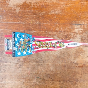 May include: A vintage pennant with a patriotic design, featuring red and white stripes, a blue section with stars and a crescent moon, and the words "Spirit of '76" and "Maryland." The pennant also includes the text "Bicentennial 1976."