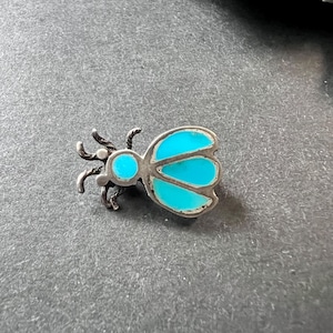 May include: A silver and turquoise butterfly pin. The butterfly has a detailed design with a round turquoise stone in the center of its body.