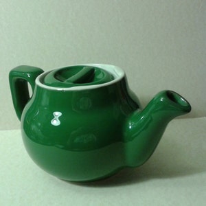 May include: A green ceramic teapot with a white lid and handle. The teapot has a rounded body and a spout on the side.