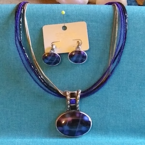 A Blue Oval Pendant Hangs from a Blue, Black Bead and Silver Chain with Pierced Earrings