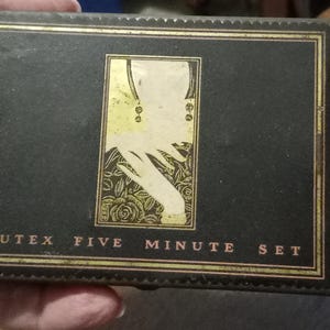 May include: A black box with gold trim and a gold and white image of a woman's hand and arm. The box has the text "Cutex Five Minute Set" on the front.
