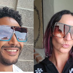 May include: Two people wearing oversized square sunglasses with brown frames. The sunglasses have a gradient lens with a blue and brown color scheme.