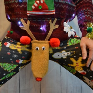 May include: A festive Christmas sweater with a reindeer-themed crotch decoration. The burgundy sweater has a green and white design, and is paired with black leggings patterned with gingerbread men, Christmas trees, and snowmen. The reindeer has googly eyes and red pom-pom antlers.