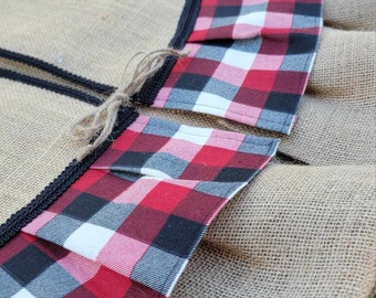 May include: A burlap Christmas tree skirt with a red, black, and white plaid trim. The trim is gathered and sewn to the burlap skirt.