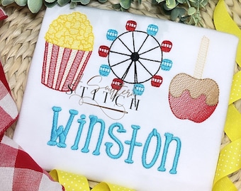 May include: White t-shirt with embroidered carnival-themed designs, including popcorn, a Ferris wheel, and a caramel apple. The name "Winston" is embroidered in blue script. The shirt is decorated with red and yellow ribbons.