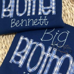 May include: Two navy blue shirts with white and blue gingham patterned text that reads "Big Brother" with a name underneath. The top shirt says "Bennett" and the bottom shirt says "Holden".