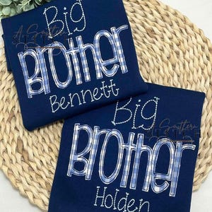 May include: Two navy blue t-shirts with white stitching. The shirts say "Big Brother" with a blue and white checkered pattern. One shirt says "Bennett" and the other says "Holden".