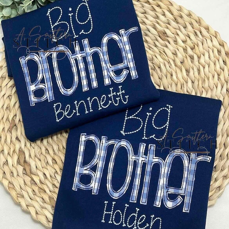 May include: Two navy blue t-shirts with white stitching. The shirts say "Big Brother" with a blue and white checkered pattern. One shirt says "Bennett" and the other says "Holden".