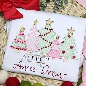 Puede incluir: Un pelele blanco con un diseño bordado de árbol de Navidad rosa y verde. El pelele tiene el texto "A Southern Stitch" y "Ava Drew" bordado.