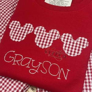 Może przedstawiać: Czerwona koszulka z trzema naszywkami Myszki Miki w biało-czerwoną kratę i imieniem "GRAYSON" wyszytym białą nicią.