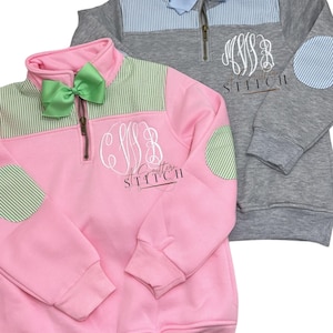 Peut inclure: Deux sweat-shirts à fermeture éclair quart pour enfants avec des panneaux de couleur contrastés et des empiècements au coude. Le sweat-shirt rose a des rayures vertes et un empiècement au coude vert, tandis que le sweat-shirt gris a des rayures bleues et un empiècement au coude bleu. Les deux sweat-shirts présentent un monogramme "C.L.B." sur le devant et le texte "A Southern Stitch" en dessous.