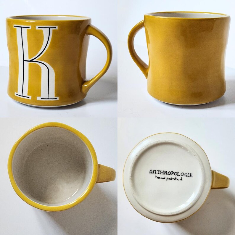 May include: Mustard yellow ceramic mug with a white letter "K" on the front. The mug has a curved handle and a white interior. The bottom of the mug has the words "ANTHROPOLOGIE hand painted".