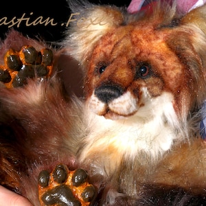Puede incluir: Un cachorro de león de peluche con pelaje marrón y canela, un pecho blanco y ojos oscuros. El cachorro de león tiene patas de color marrón anaranjado con almohadillas negras. La imagen incluye el texto "@sebastian.Foxe".