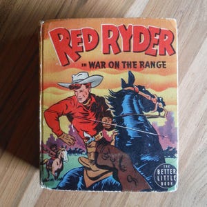 May include: A vintage paperback book cover featuring a red and white illustration of Red Ryder on horseback. The title reads "Red Ryder in War on the Range" and the book is labelled "The Better Little Book".