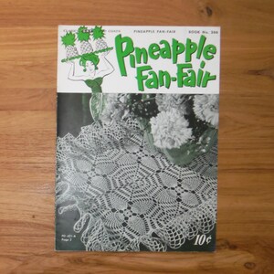 Op de afbeelding: Een vintage boekomslag getiteld "Pineapple Fan-Fair" met een groen en wit ontwerp. De omslag toont een vrouw die ananassen vasthoudt en een gehaakte kleed is zichtbaar. De prijs is 10¢.