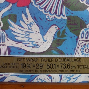 May include: A sheet of blue and white gift wrap with a floral pattern and white doves. The wrap is 19 3/4 inches by 29 inches and is 7.95 square feet. The text on the label reads "Gift Wrap Papier d'Emballage 60&cent; 2 Sheets Each Sheet 19 3/4" x 29" 50.1 x 73.6 cm Total 7.95 sq ft .737 m&sup2; Rust Craft Ltd., Scarborough, Ontario, M1P 3C9."