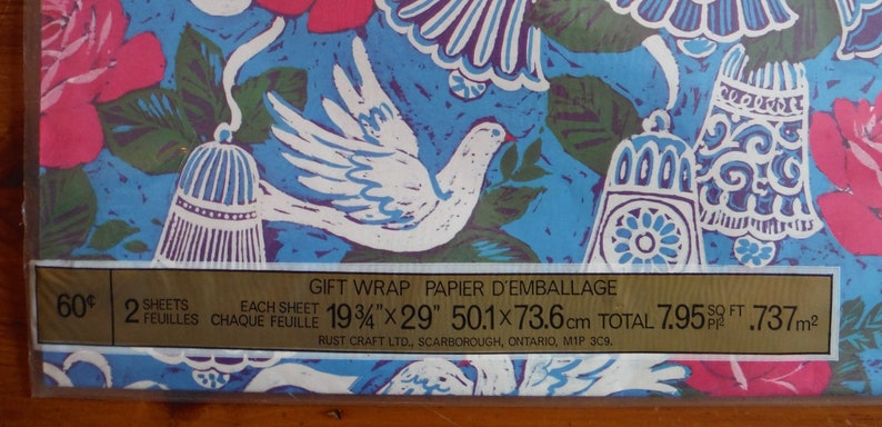May include: A sheet of blue and white gift wrap with a floral pattern and white doves. The wrap is 19 3/4 inches by 29 inches and is 7.95 square feet. The text on the label reads "Gift Wrap Papier d'Emballage 60&cent; 2 Sheets Each Sheet 19 3/4" x 29" 50.1 x 73.6 cm Total 7.95 sq ft .737 m&sup2; Rust Craft Ltd., Scarborough, Ontario, M1P 3C9."