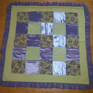 May include: A patchwork quilt with a green background and purple and floral patterned squares. The quilt has a purple ruffled border.