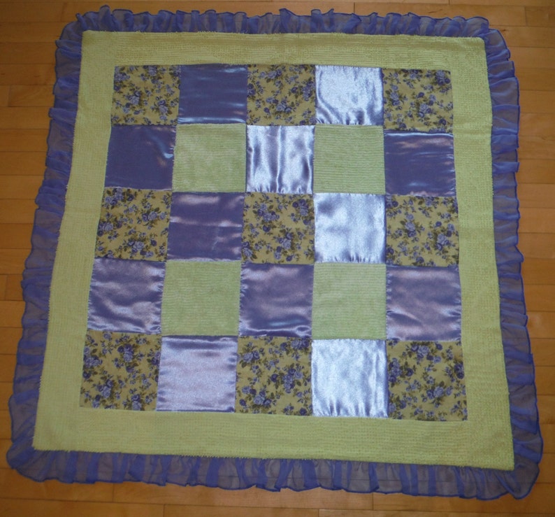 May include: A patchwork quilt with a green background and purple and floral patterned squares. The quilt has a purple ruffled border.
