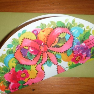 Peut inclure: Une carte verte avec un motif floral color&eacute; comprenant un n&oelig;ud rose, des feuilles vertes et des fleurs rouges, jaunes et bleues. La carte est pli&eacute;e en deux et le motif est sur le devant.